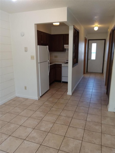 Kitchen with a textured ceiling, dark brown cabinets, light tile patterned floors, and white appliances