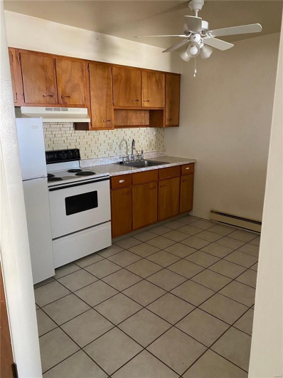 Kitchen with white appliances, tasteful backsplash, a baseboard heating unit, and sink