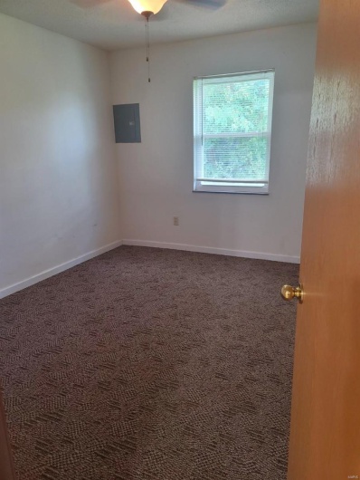 Carpeted empty room featuring ceiling fan and electric panel