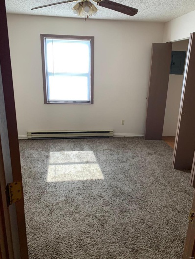 Empty room featuring carpet flooring, a textured ceiling, a baseboard radiator, and electric panel