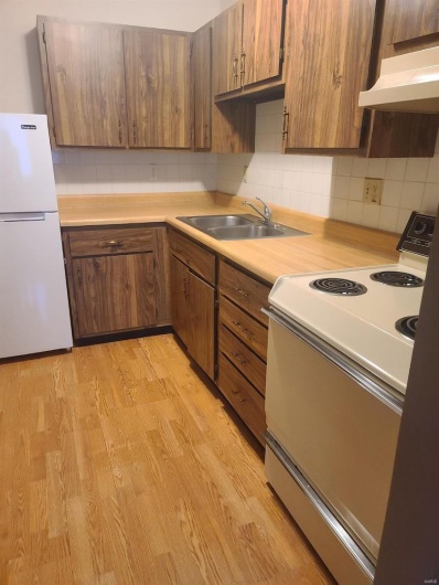 Kitchen featuring stove, backsplash, sink, white refrigerator, and light hardwood / wood-style floors