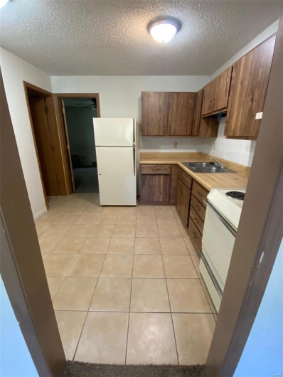 Kitchen featuring sink, white appliances, a textured ceiling, and light tile patterned floors