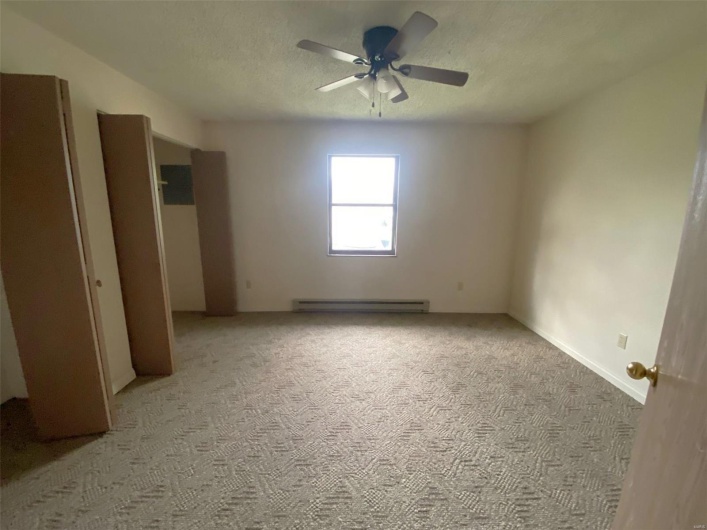Unfurnished bedroom featuring ceiling fan, light colored carpet, a textured ceiling, and a baseboard heating unit