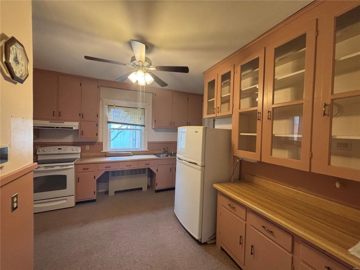 Kitchen with white appliances, light colored carpet, ceiling fan, and sink