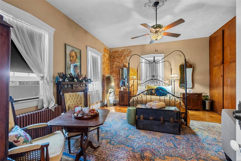 Bedroom featuring hardwood / wood-style floors, brick wall, ceiling fan, and radiator