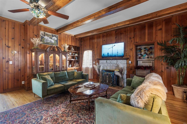 Living room with a fireplace, hardwood / wood-style flooring, beamed ceiling, and wooden walls