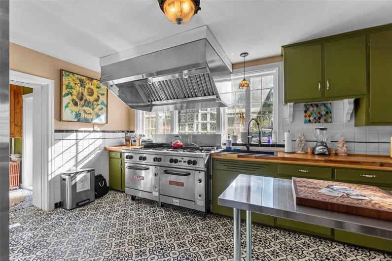 Kitchen with butcher block countertops, high end stainless steel range, extractor fan, green cabinets, and sink
