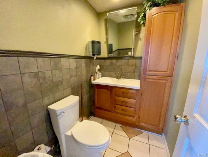 Bathroom featuring tile patterned floors, vanity, tile walls, and toilet
