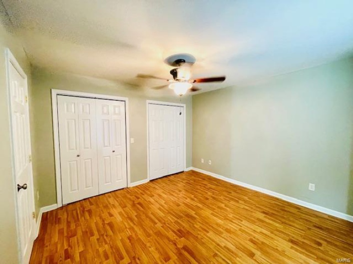 Unfurnished bedroom featuring multiple closets, ceiling fan, and wood-type flooring
