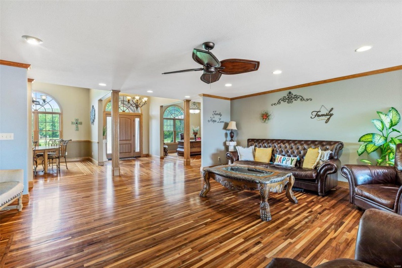 Living room with wood-type flooring, ceiling fan with notable chandelier, and crown molding