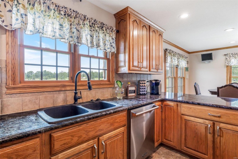 Kitchen featuring sink, stainless steel dishwasher, dark stone counters, decorative backsplash, and ornamental molding