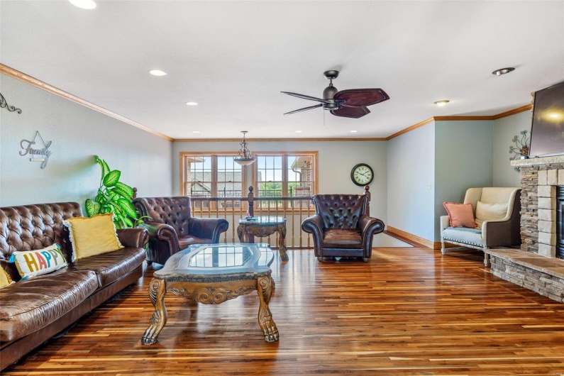 Living room with ceiling fan, a stone fireplace, dark wood-type flooring, and crown molding