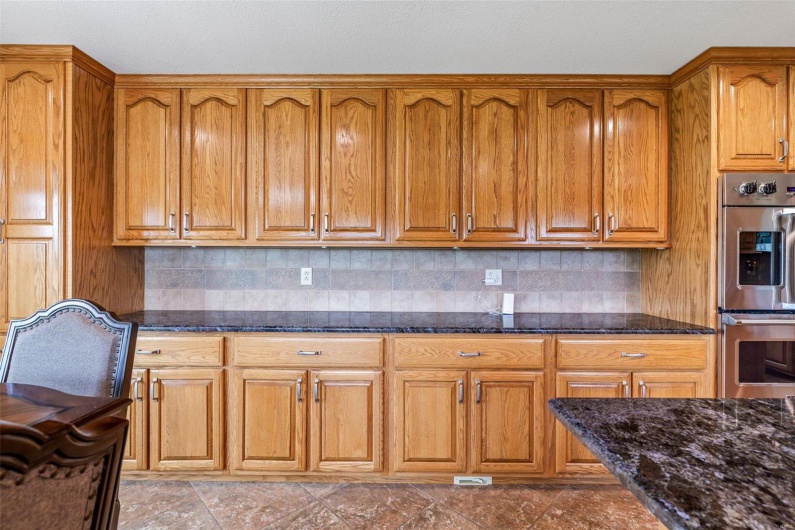 Kitchen with tasteful backsplash, light tile patterned flooring, double oven, and dark stone counters