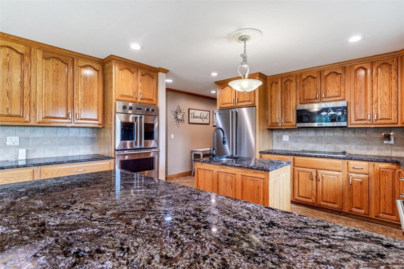 Kitchen featuring backsplash, ornamental molding, stainless steel appliances, pendant lighting, and a center island with sink