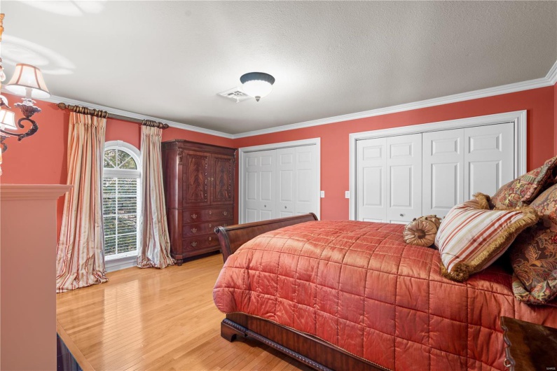 Bedroom with a textured ceiling, light hardwood / wood-style floors, multiple closets, and ornamental molding