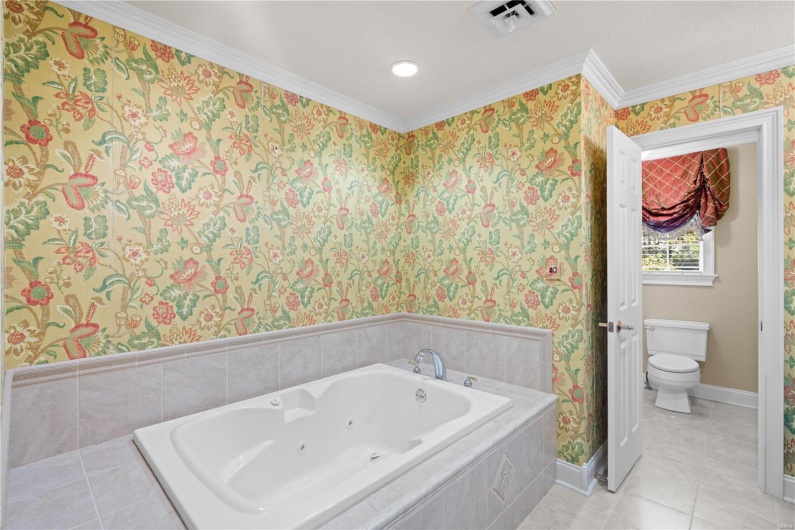 Bathroom featuring tile patterned floors, a relaxing tiled tub, toilet, and crown molding