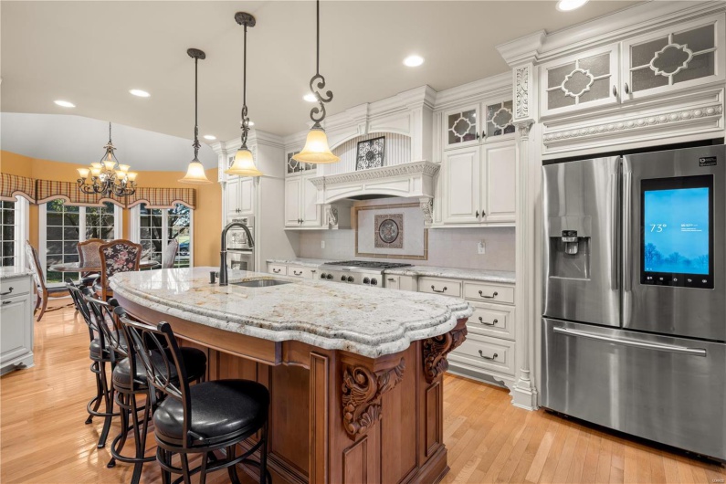 Kitchen with white cabinets, stainless steel appliances, hanging light fixtures, and an island with sink