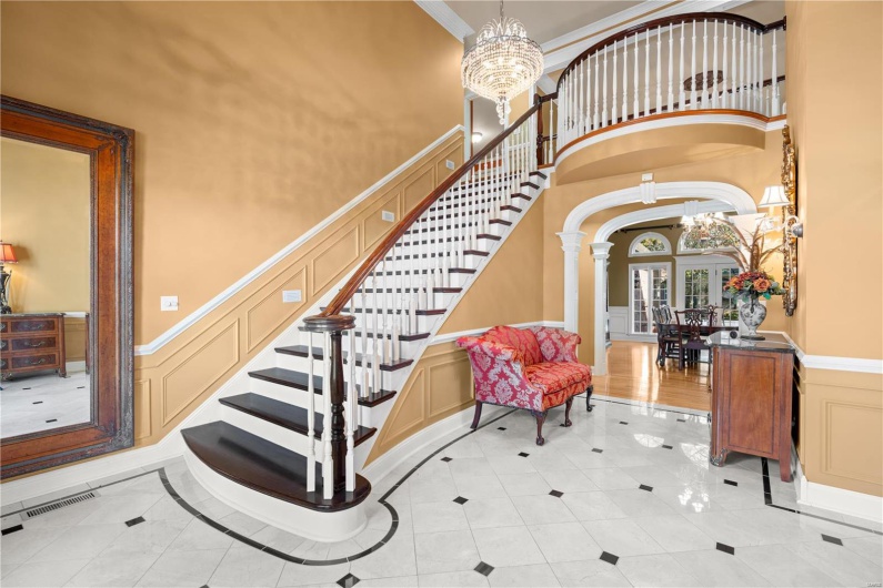 Stairs with french doors, a towering ceiling, decorative columns, crown molding, and an inviting chandelier