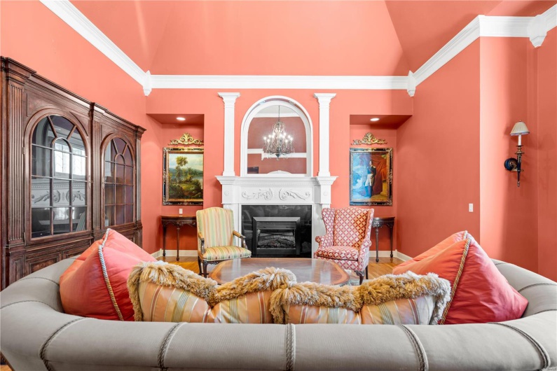 Living room featuring an inviting chandelier, a high end fireplace, high vaulted ceiling, crown molding, and hardwood / wood-style floors