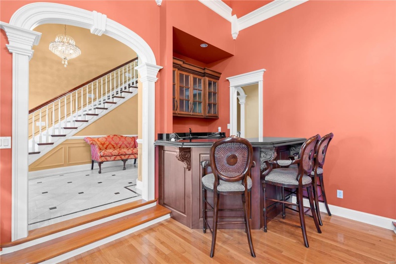 Bar featuring a chandelier, a towering ceiling, light hardwood / wood-style floors, and ornamental molding