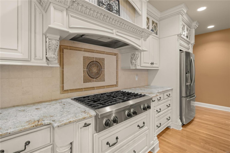 Kitchen with premium range hood, backsplash, white cabinets, and appliances with stainless steel finishes
