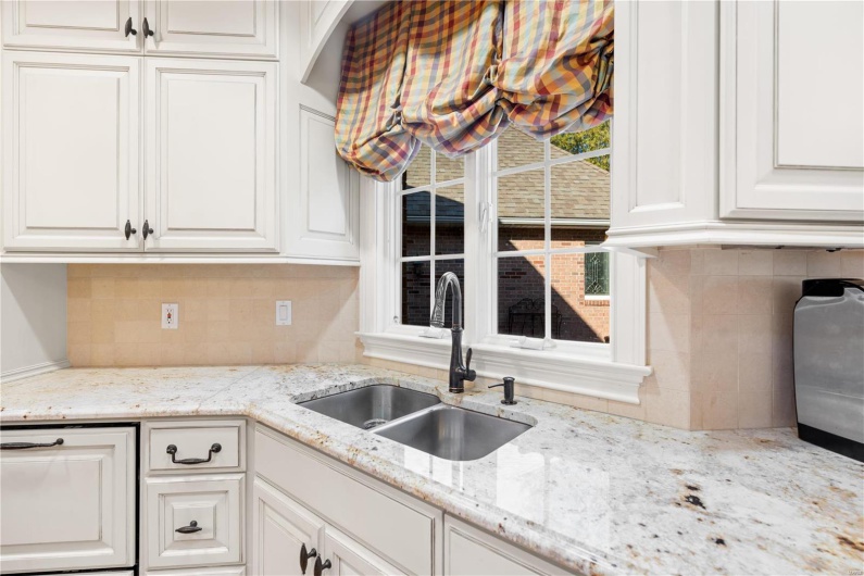 Kitchen featuring backsplash, light stone countertops, sink, and white cabinets