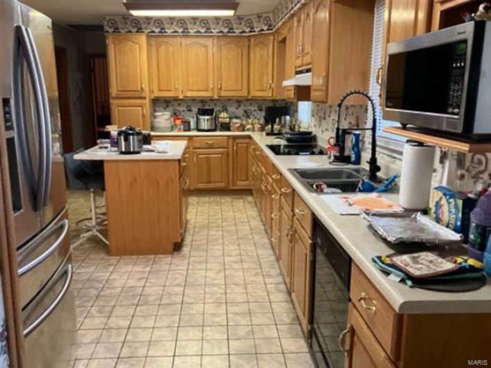 Kitchen featuring a center island, black appliances, sink, light tile patterned floors, and a breakfast bar area