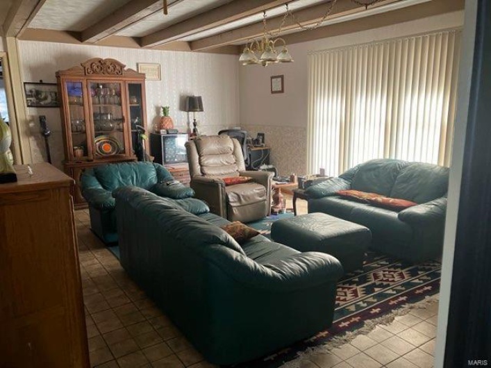Living room with tile patterned flooring, a notable chandelier, and beam ceiling