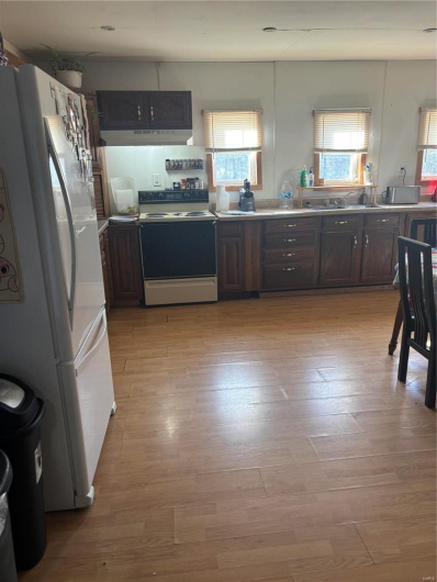Kitchen with dark brown cabinets, refrigerator, stove, and a wealth of natural light