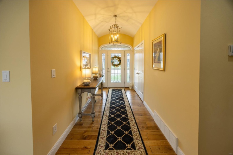 Front foyer with wooden flooring, vaulted ceiling, and chandelier.