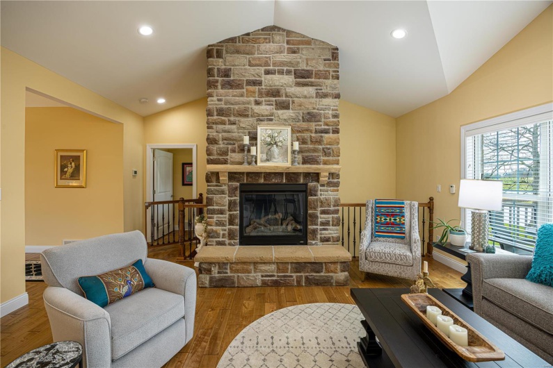 Living room featuring a fireplace, wood flooring, and vaulted ceiling with view of lake in backyard.