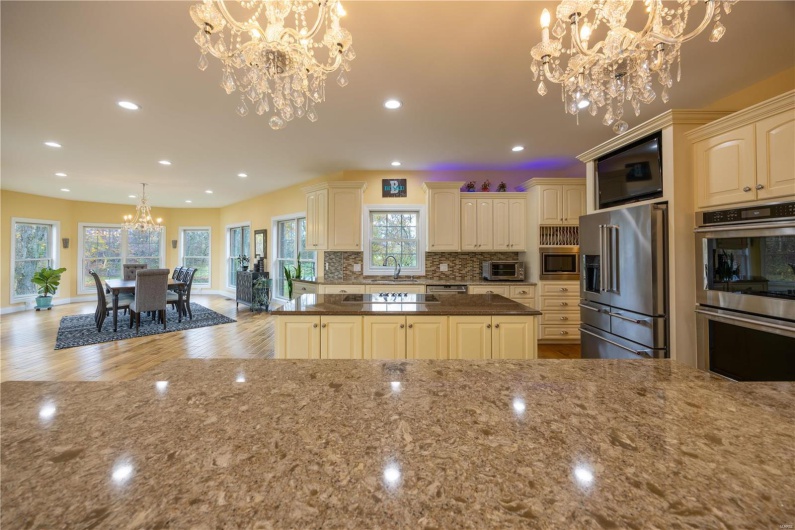 Kitchen featuring sink, cooktop, hanging chandeliers, appliances with stainless steel finishes, and light hardwood flooring.