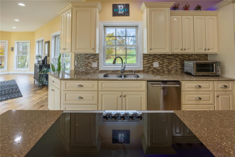 Kitchen featuring dishwasher, dark stone countertops, light wood flooring, and sink.