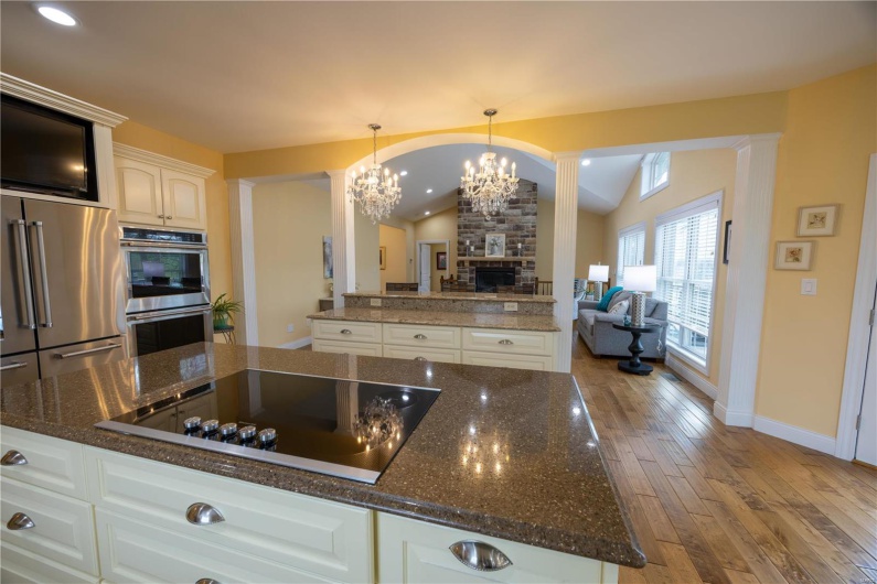 Kitchen with stainless steel appliances, breakfast bar, stone fireplace, light hardwood flooring, vaulted ceiling, and white custom cabinets.