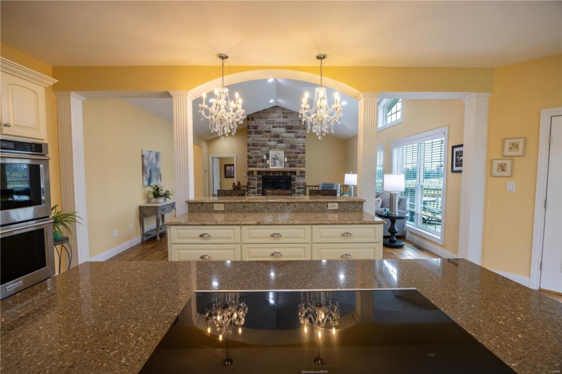 Kitchen with cooktop, breakfast bar, hardwood flooring, vaulted ceiling, hanging chandeliers, and ornate columns.