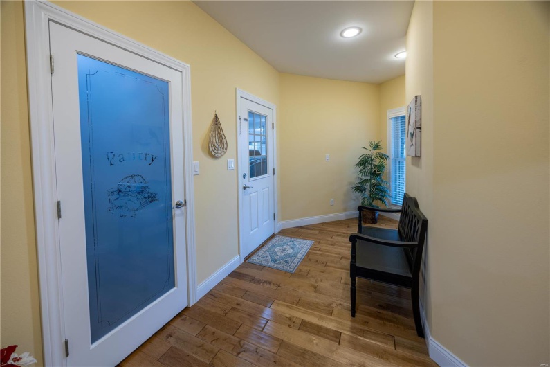 Entry to home from garage, with pantry to left and light hardwood flooring.