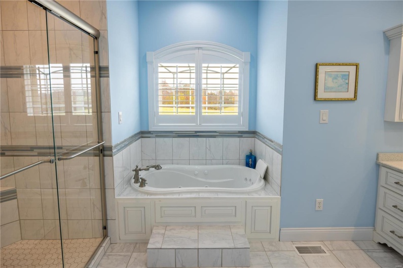 Bathroom with marble patterned flooring, vanity, and separate shower and bathtub.