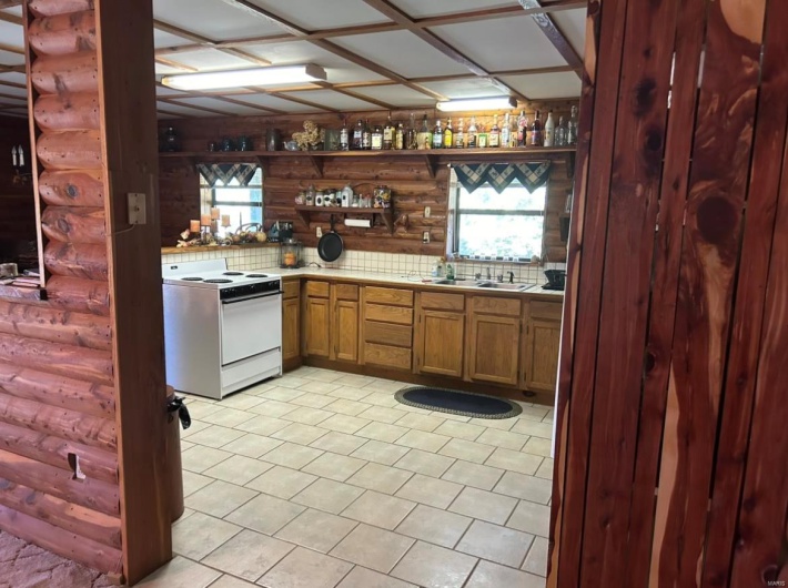 Kitchen featuring log walls, decorative backsplash, white stove, and sink