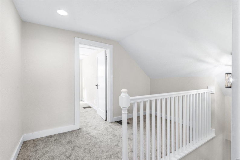Hallway with lofted ceiling and light carpet