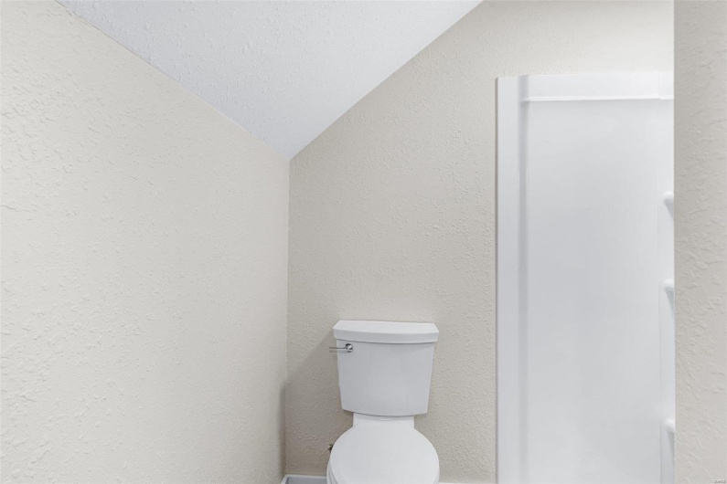 Bathroom with toilet, a textured ceiling, and vaulted ceiling