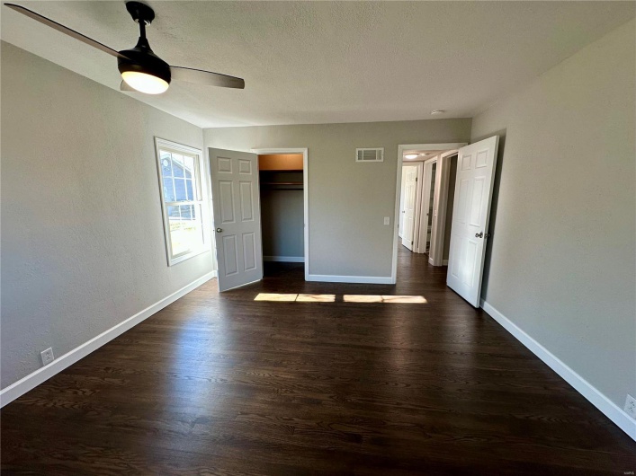 Unfurnished bedroom featuring a walk in closet, ceiling fan, a closet, and dark wood-type flooring