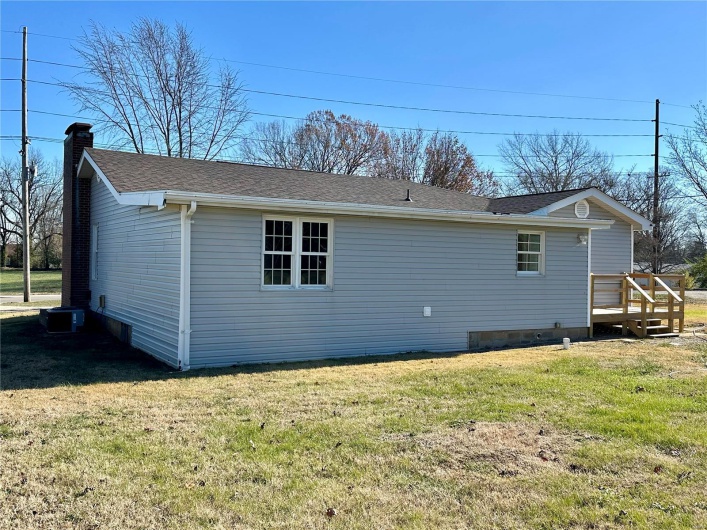 Rear view of house with central air condition unit, a wooden deck, and a lawn