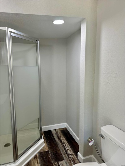 Bathroom with wood-type flooring, an enclosed shower, and toilet