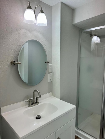 Bathroom with a textured ceiling, vanity, and a shower with shower door