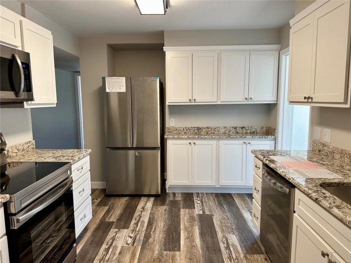 Kitchen with light stone counters, white cabinets, dark wood-type flooring, and appliances with stainless steel finishes