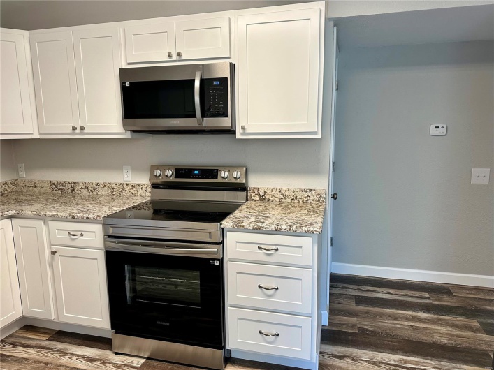 Kitchen with white cabinets, appliances with stainless steel finishes, light stone counters, and dark wood-type flooring