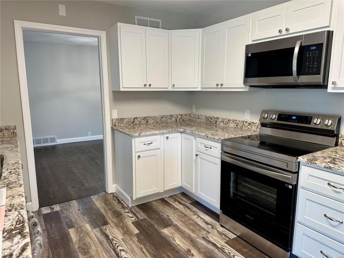 Kitchen with light stone countertops, white cabinets, dark wood-type flooring, and appliances with stainless steel finishes