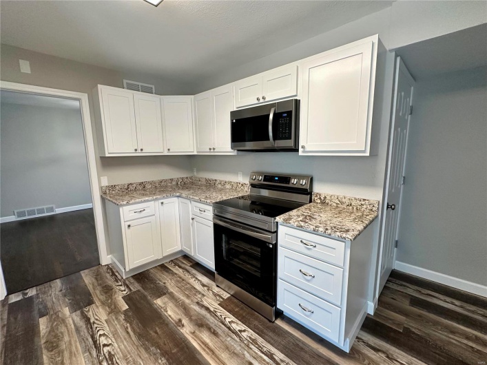 Kitchen featuring dark hardwood / wood-style flooring, stainless steel appliances, white cabinetry, and light stone counters