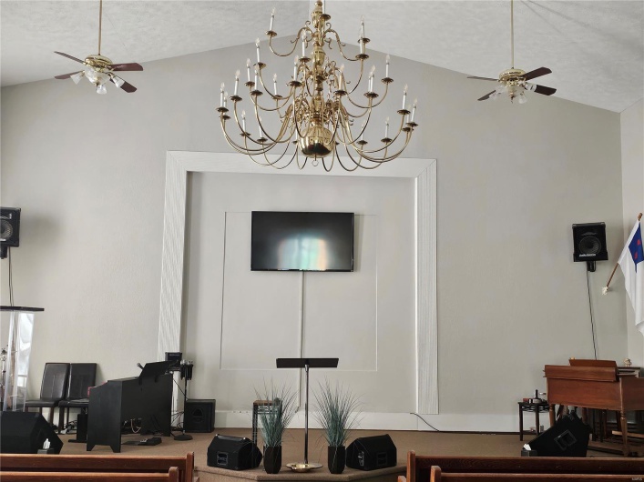 Living room with a textured ceiling, ceiling fan with notable chandelier, and high vaulted ceiling
