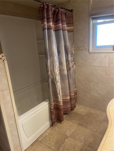 Full bathroom with shower / bath combo and stone tile flooring